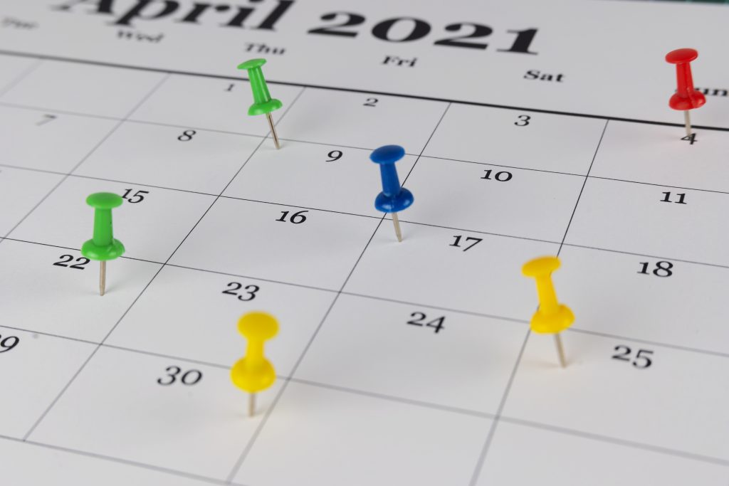 A calendar with colorful thumbtacks marking important dates as reminders.